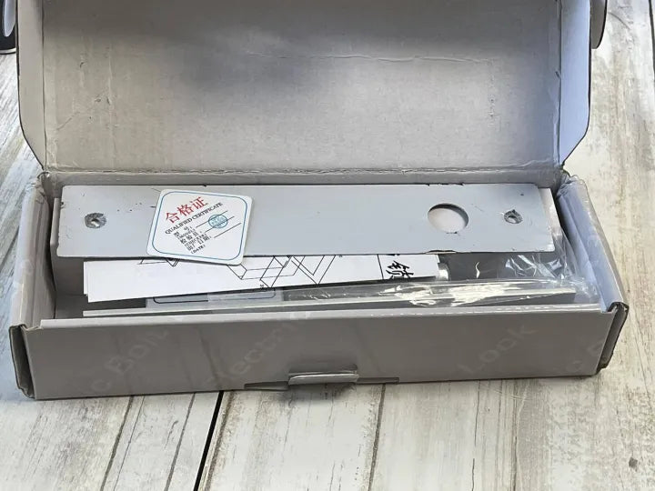 Open box of the sliding door lock kit, including the bolt lock, mounting hardware, and a qualified certificate.

