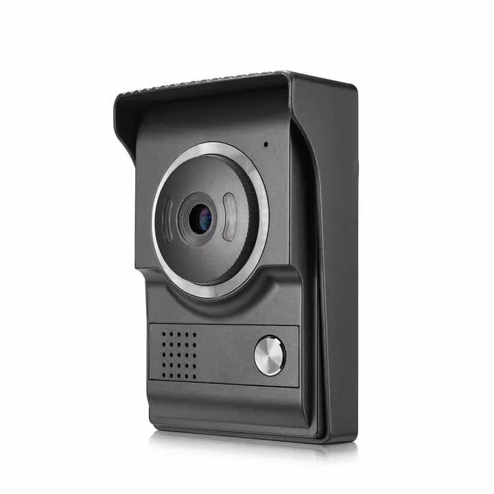 A front-angle shot of the AMOCAM outdoor unit for a video intercom doorbell. The unit is dark gray with a protective hood, featuring a prominent circular camera lens with a silver trim, a speaker grille, and a circular metallic call button at the bottom. The sleek design is optimized for outdoor mounting