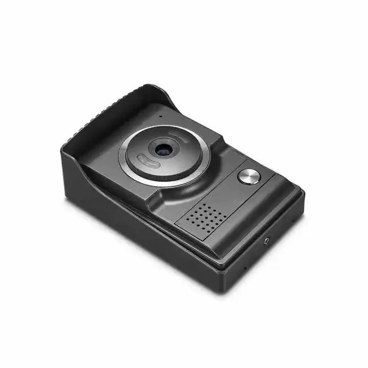 A slightly elevated perspective view of the compact AMOCAM outdoor video doorbell unit. The dark gray casing with a protective top lip clearly shows the main camera lens with its silver accent, a speaker grill below it, and the integrated call button. This angle emphasizes its robust and streamlined design for exterior use.